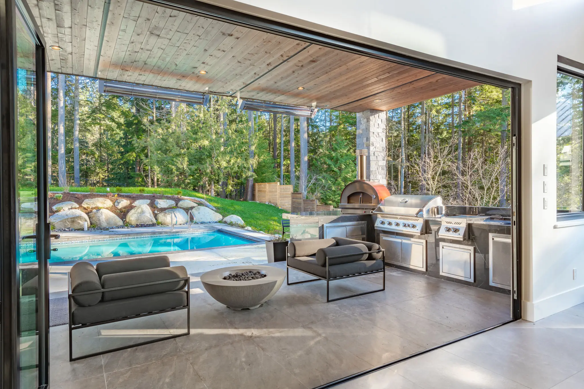 Modern outdoor living space with pool, fireplace, and grill area.