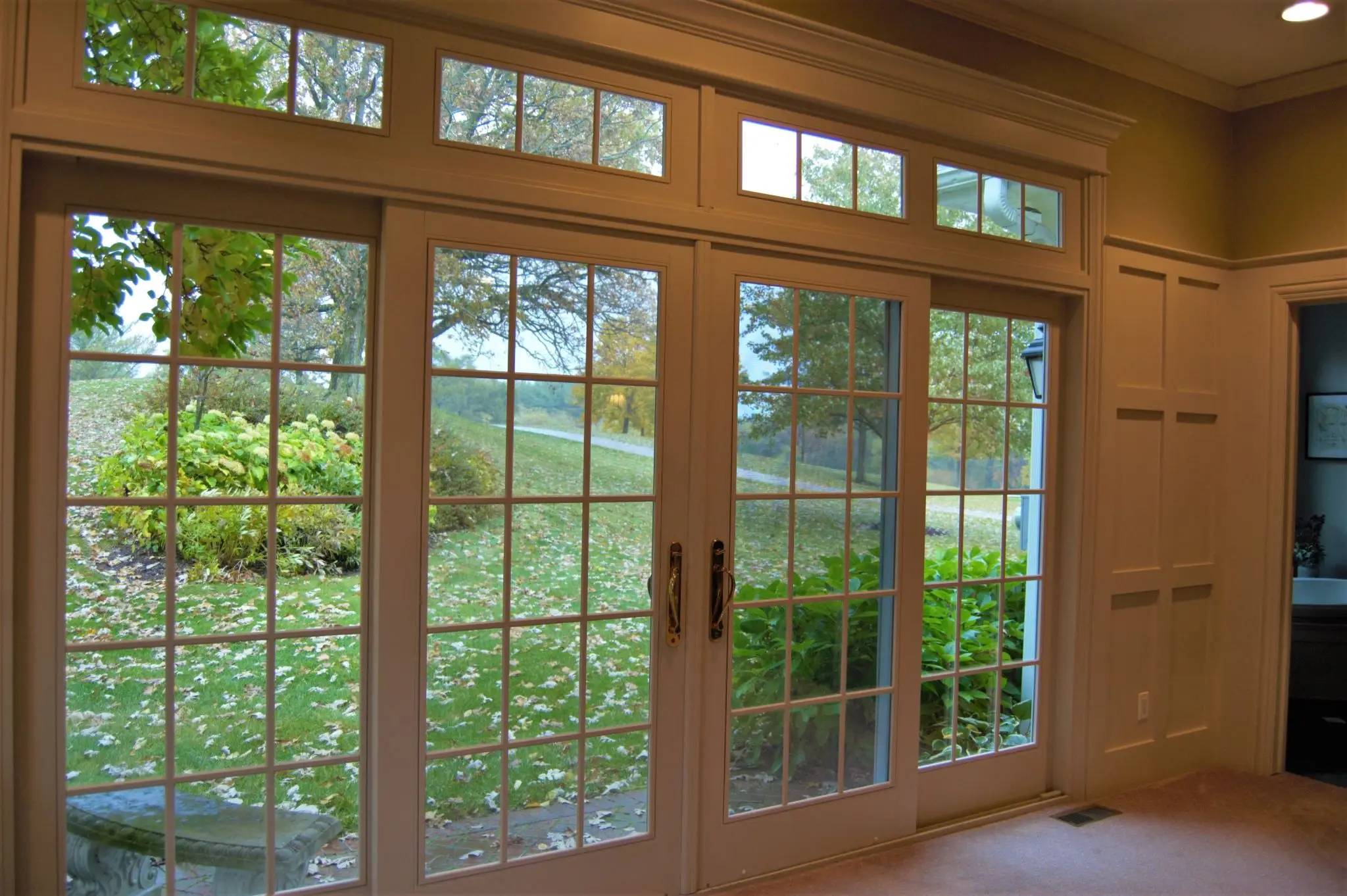 View of a scenic lake and greenery through large glass doors with wooden frames.