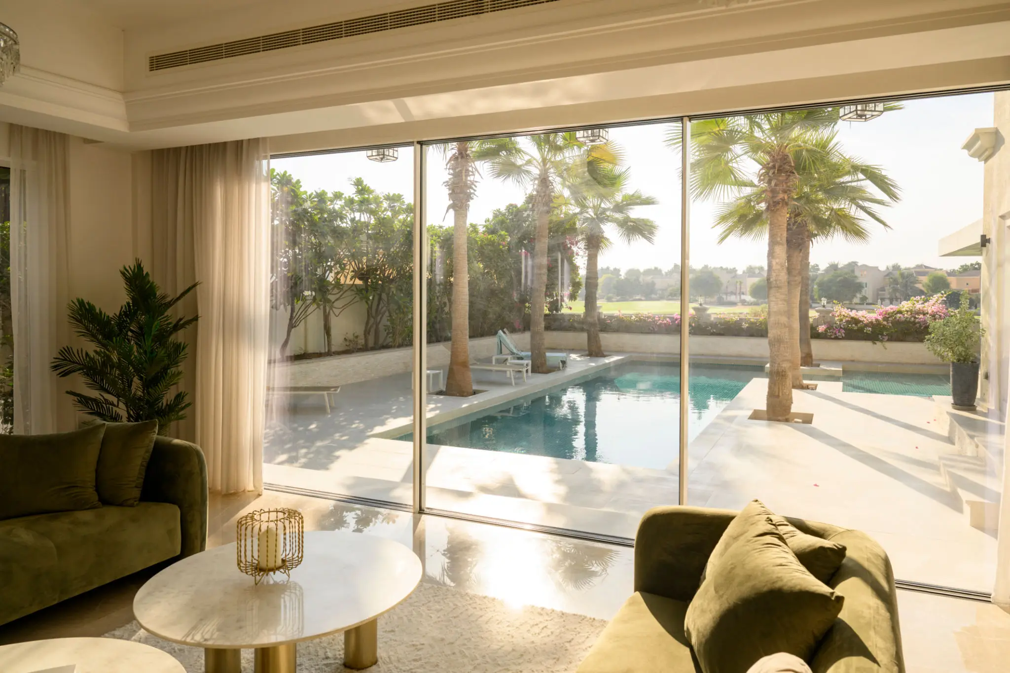 Modern living room with large sliding doors opening to a pool and palm trees.